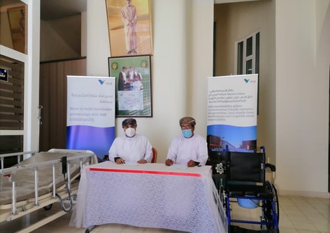 Image of two men sitting behind a table. On one side is a hospital bed and on the other a wheelchair.