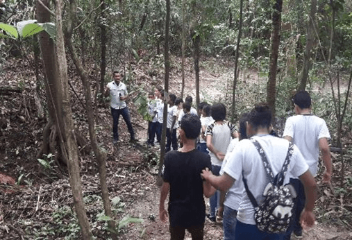 Em uma trilha, diversos estudantes prestam atenção na fala de um empregado Vale, que está à frente do grupo.