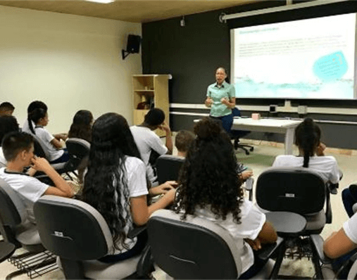 Em uma sala de aula, alunos prestam atenção na fala de uma empregada Vale, que está à frente da turma.