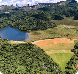 Imagem aérea da barragem 5-MAC. Há bastante vegetação ao redor e um lago no topo da estrutura.