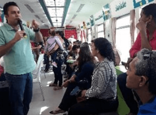 Um empregado Vale, usando um microfone, discursa para diversas pessoas dentro do vagão de um trem.