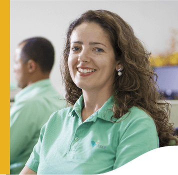 A woman smiling in an office environment. She has her hair down and wears light green shirt with Vale logo.