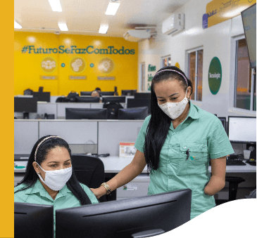 Two female Vale employees chat in an office. One is seated and the other is standing. Both are wearing masks.