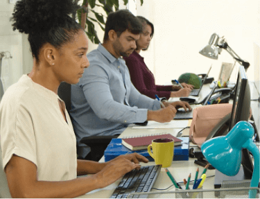 Foto de um ambiente de escritório com duas mulheres e um homem trabalhando lado a lado em suas mesas.