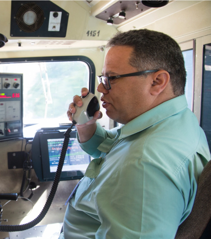 Vale employee speaks in a microphone in the cabin of a train. He wears uniform and glasses