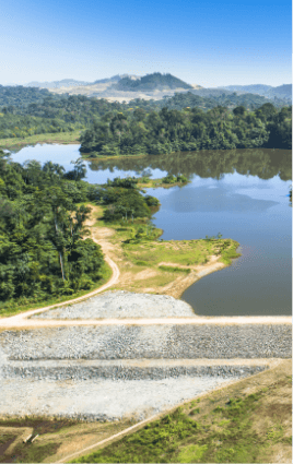 Foto de uma barragem eliminada com pedras, um rio, caminho de terra e vegetação ao redor