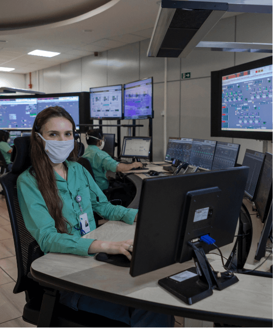 Vale employee wearing a protective mask, uniform, and badge. She is sitting in a room full of computers.