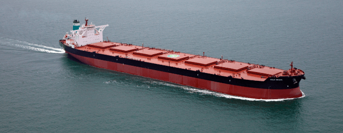 Image of a large cargo ship. It is red and has a black stripe, and is sailing on the high seas.