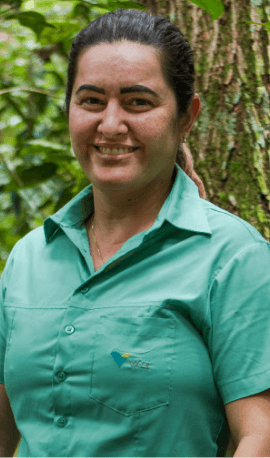 Mulher sorrindo em uma área arborizada. Ela está usando camisa verde clara e o cabelo preso para trás.