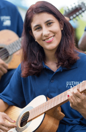 Uma mulher toca violão, enquanto sorri para câmera.
