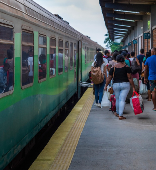 Diversas pessoas aguardam a chegada do trem na estação Intendente Câmara. As pessoas estão com malas e mochilas.