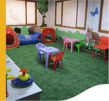 Sala fechada com grama sintética e ilustrações de animais nas paredes. O local conta com brinquedos infantis.