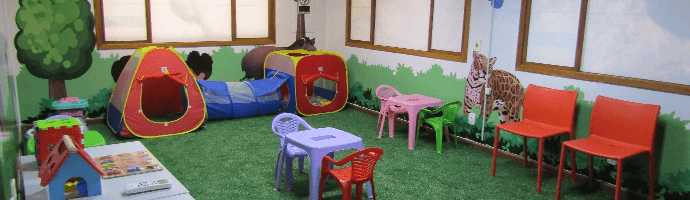 A closed room with synthetic grass and illustrations of animal on the walls. There are children's toys in the place.