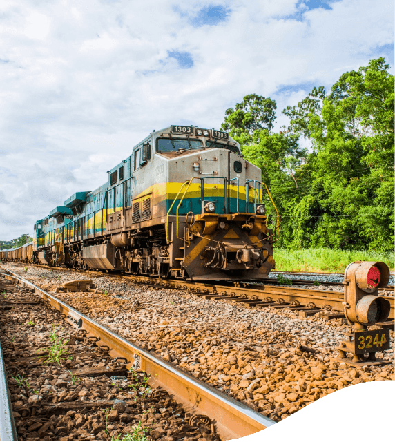 Trem de carga Vale trafegando por um trilho cheio de pedras. Oo fundo é possível ver algumas árvores.