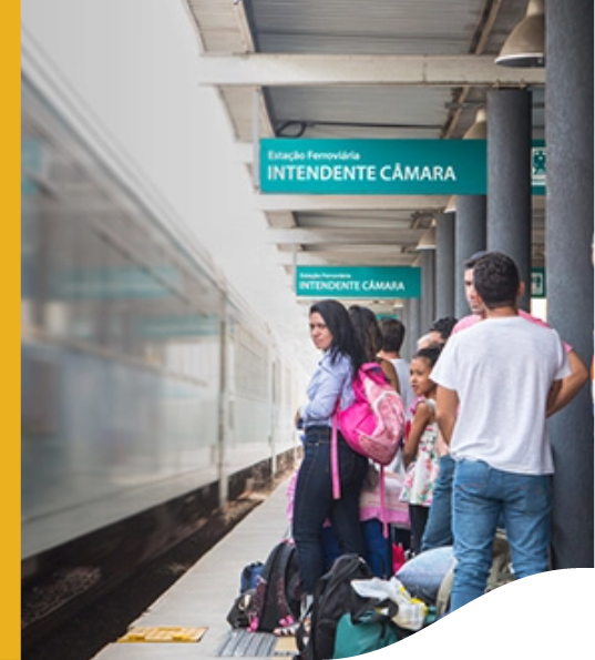 Several people are waiting for the train to arrive at the Intendente Câmara station. The people are with suitcases and backpacks.