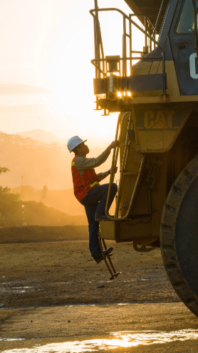 Image of an employee, wearing a white helmet and orange vest, climbing onto a yellow truck