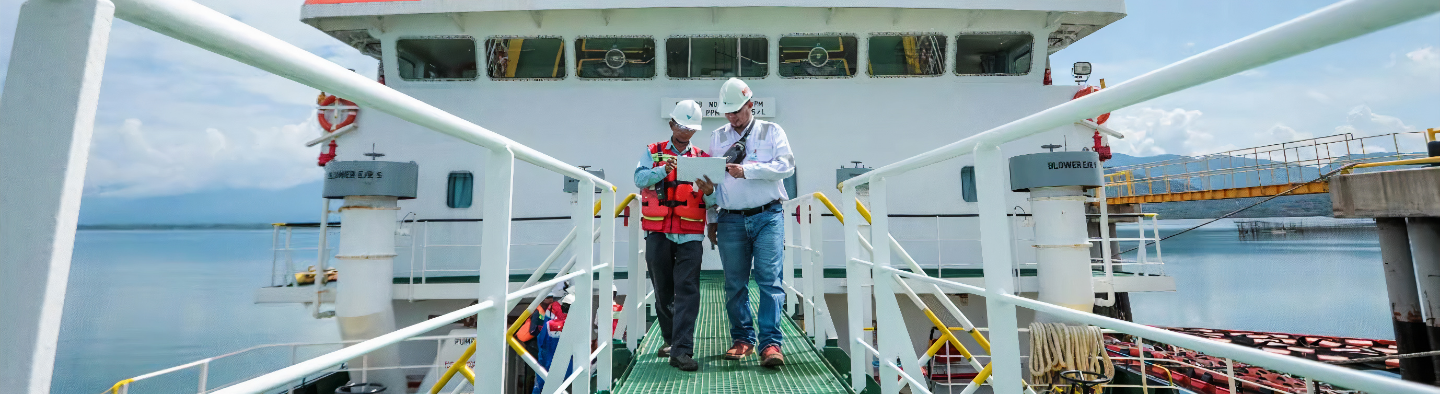 Two men were walking along a footbridge connected to a ship. They both looked at a piece of paper in the hand of one of the men.