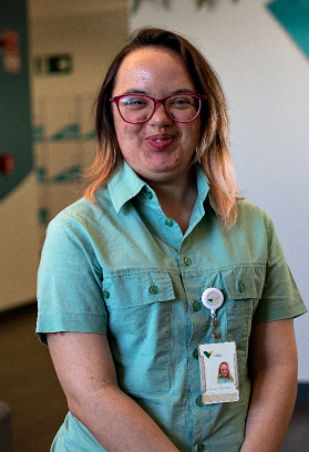 Uma mulher, com síndrome de Down, está sorrindo para foto. Ela usa uniforme e crachá da Vale.