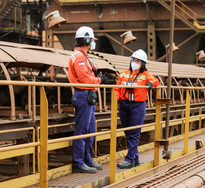 A man and woman are chatting in an open area. They are both wearing masks, helmets, goggles and gloves.