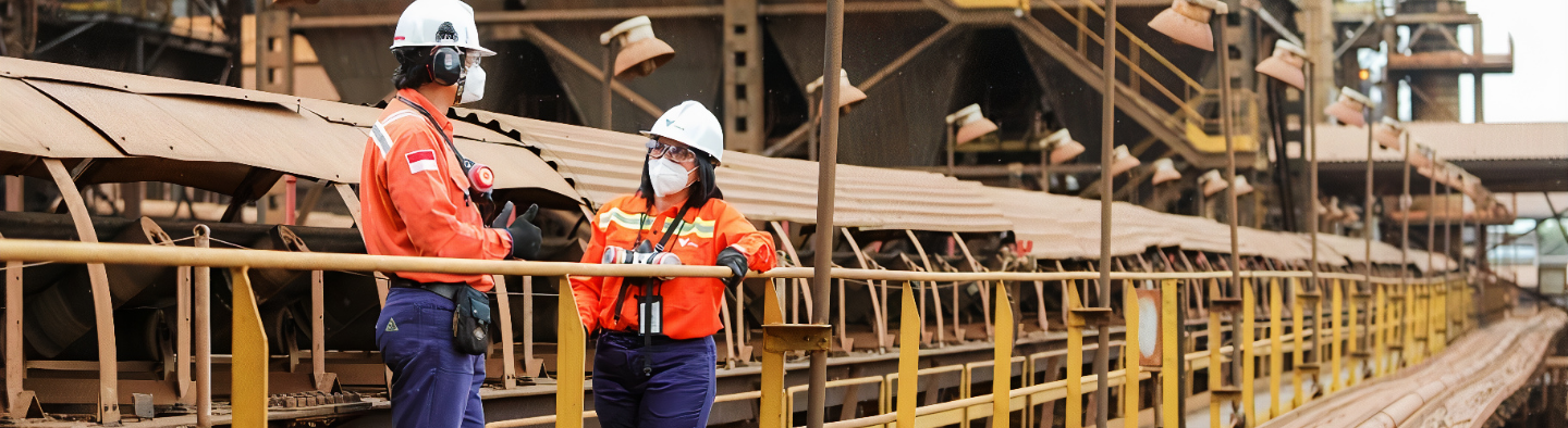 A man and woman are chatting in an open area. They are both wearing masks, helmets, goggles and gloves.