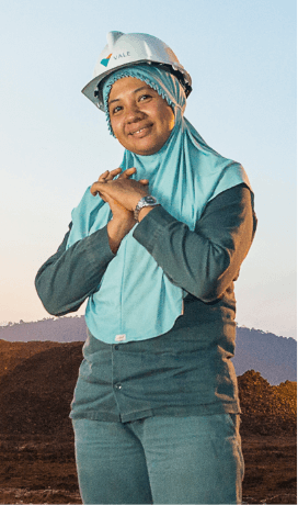 a woman is wearing a hijab and a protective helmet. She is in an outdoor area, where it is possible to see mountains in the background.