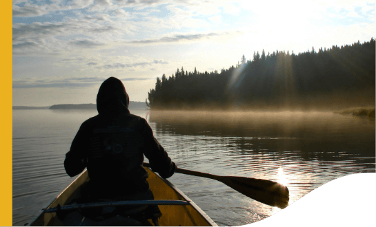 A man is on his back sailing a boat. There is a lot of vegetation in the background.