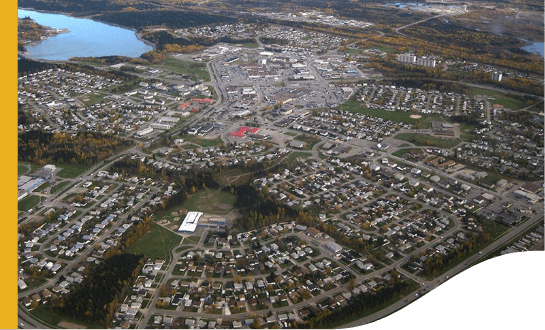 Aerial view of Thompson. In the place, there are several houses and a lot of grass space, except the center, where there is little green area. In the upper right corner of the screen, it is possible to see a lake.