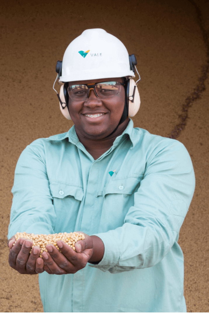 Homem negro sorrindo e usando uniforme verde, óculos de proteção e capacete com o logotipo da Vale.