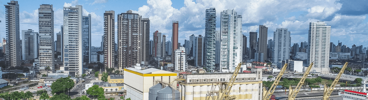 Photo of a city with several tall buildings, streets and some cranes next to a warehouse.