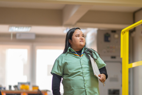 A disabled woman is holding a briefcase under her arm and smiling for a photo. She is wearing a Vale uniform.