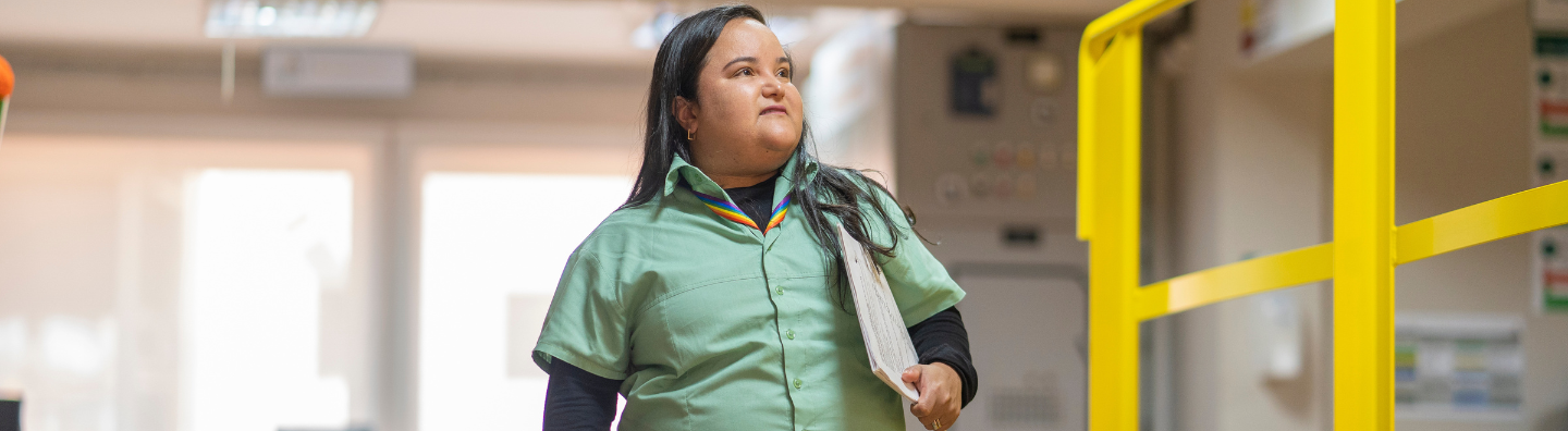 A disabled woman is holding a briefcase under her arm and smiling for a photo. She is wearing a Vale uniform.