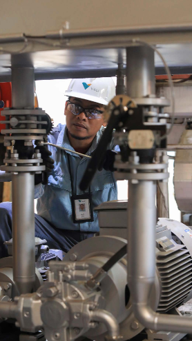 A Vale employee is looking at a piece of equipment. He is wearing a hard hat, safety glasses and a name tag around his neck.