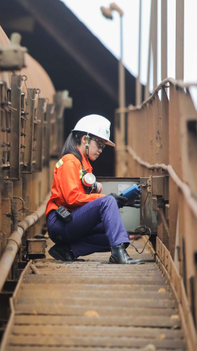 Seorang wanita berada di atas jembatan, menangani peralatan. Ia mengenakan seragam Vale, topi baja, serta sarung tangan dan kacamata pelindung.