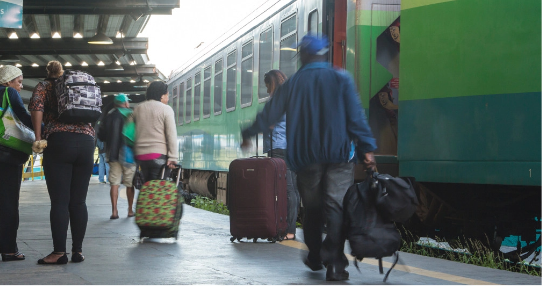 Passengers with bags and suitcases circulate on the train platform, while the locomotive is parked.