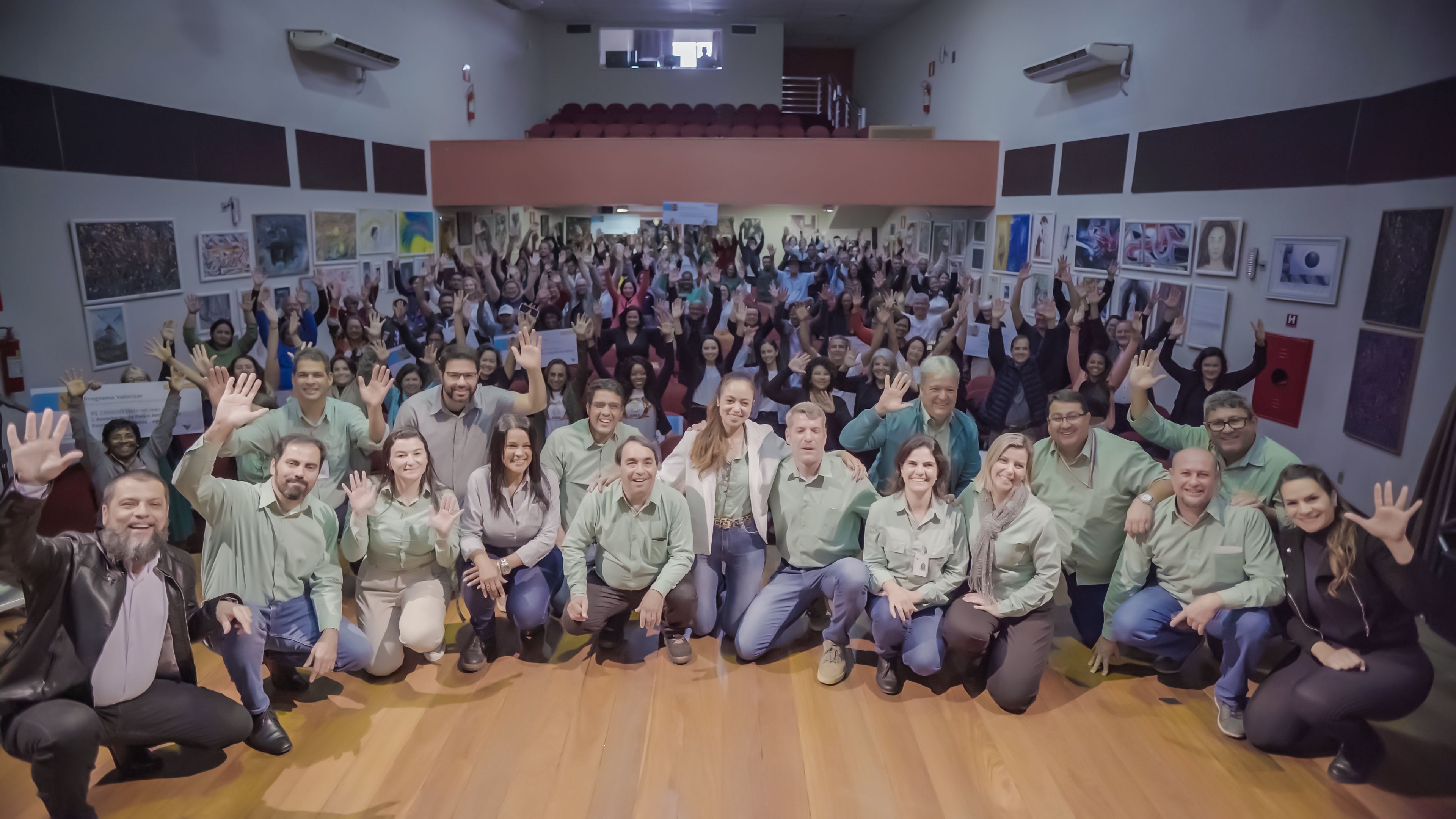 Diversas pessoas reunidas em um auditório posam para foto, a maioria deles está com as mãos para cima e usa uniforme Vale.