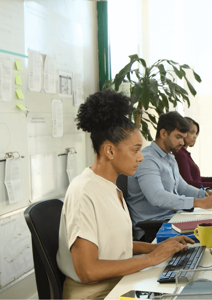 Foto de um ambiente de escritório com duas mulheres e um homem trabalhando lado a lado em suas mesas.