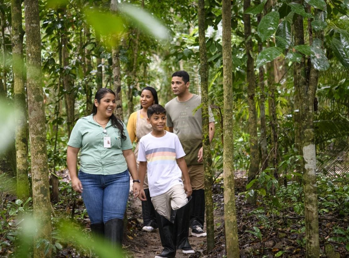 Uma empregada Vale caminha junto com uma familia por um espaço arborizado