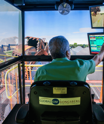 Vale employee, sitting with his back to the photo, remotely operating a piece of equipment. He is touching one of the two screens in front of him. In the background, you can see a large piece of machinery.