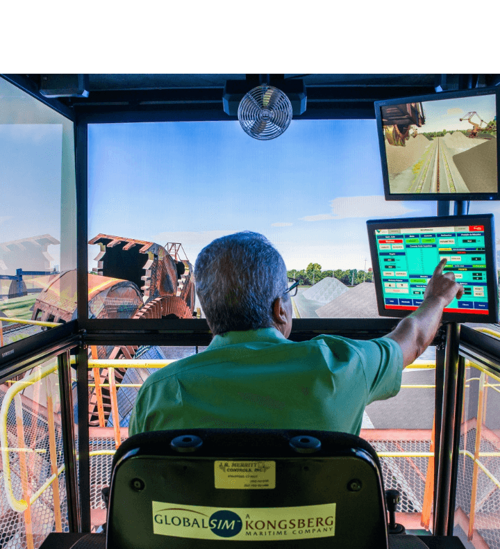 Vale employee, sitting with his back to the photo, remotely operating a piece of equipment. He is touching one of the two screens in front of him. In the background, you can see a large piece of machinery.