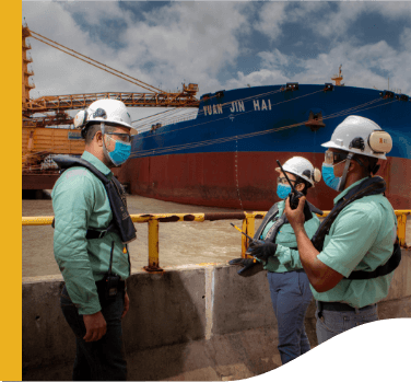 Three Vale employees are talking in front of a ship. All wear protective equipment