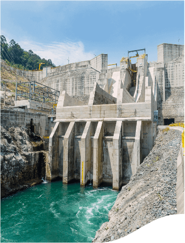 Image of a hydropower plant. There is a large concrete structure, similar to a high wall with some columns, occupying most of the image. Underneath there is water.