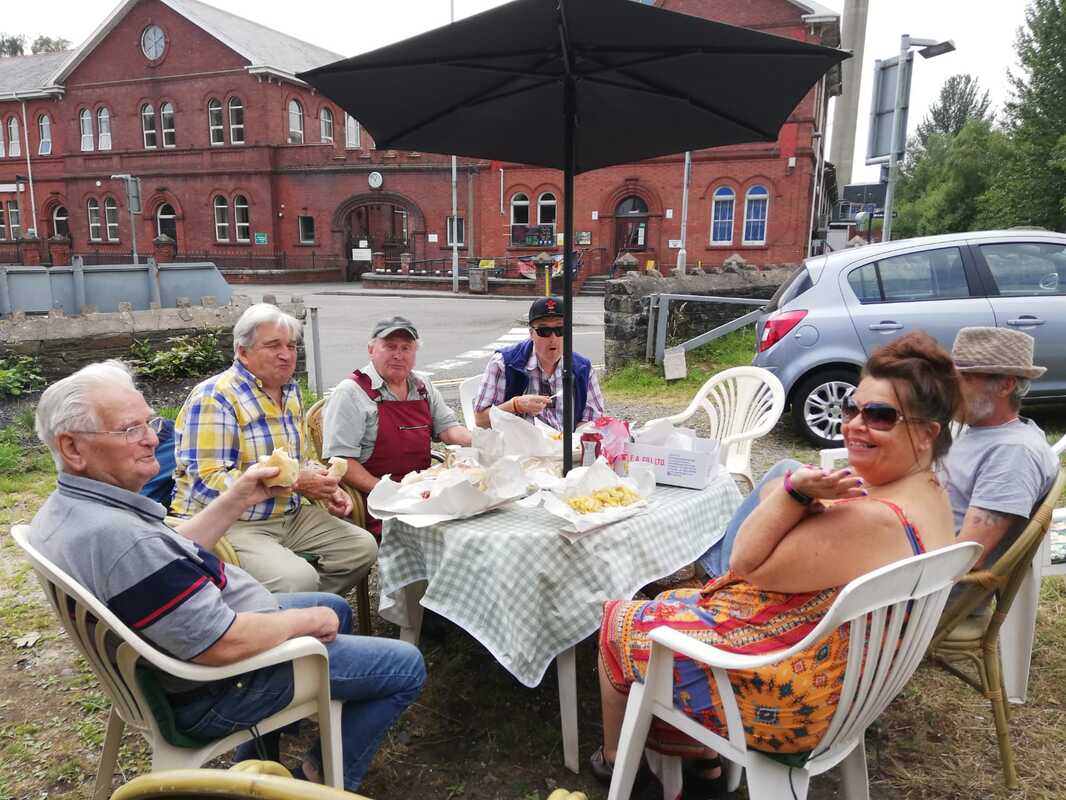 Um grupo de pessoas sentadas à volta de uma mesa em frente às operações de Clydach