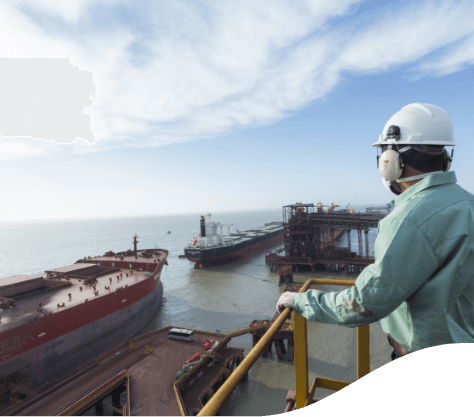 A Vale employee, wearing a green uniform, helmet and protective gloves, observes a port with two docked cargo ships.