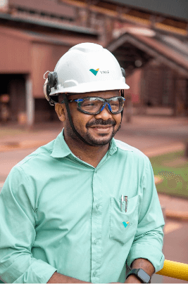 Belly to head shot of a smiling bearded man wearing Vale's green uniform, with helmet and glasses leaning on a railing.