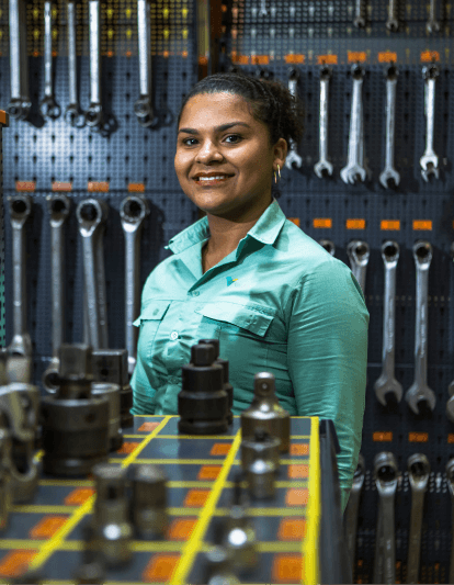 Vale Employee smiling for a photo. She is wearing the green uniform, and in the background you can see tools hanging on the wall.