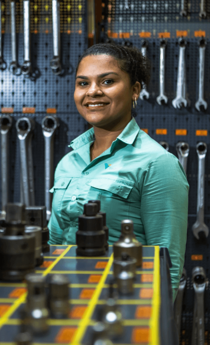 Vale Employee smiling for a photo. She is wearing the green uniform, and in the background you can see tools hanging on the wall.