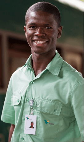 A black man smiling in an operational space. He is wearing a light green shirt and a badge.