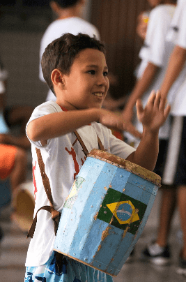 Uma criança toca um tambor, que tem a bandeira do Brasil desenhada.