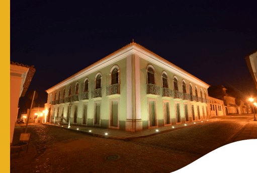 Imagem noturna do Centro Cultural Vale Maranhão. A arquitetura remete há um casarão antigo, repleto de portas, janelas e sacadas. As paredes são verde claras.
