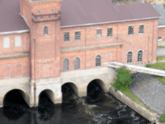 Photo of High Falls small hydropower plant. A shed structure with bricks and windows, and under the structure three water passages.